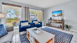 A living room with a sofa, two blue armchairs, a coffee table, a TV, and a wooden console. - Nautical Watch E-3 (Panama City Beach)