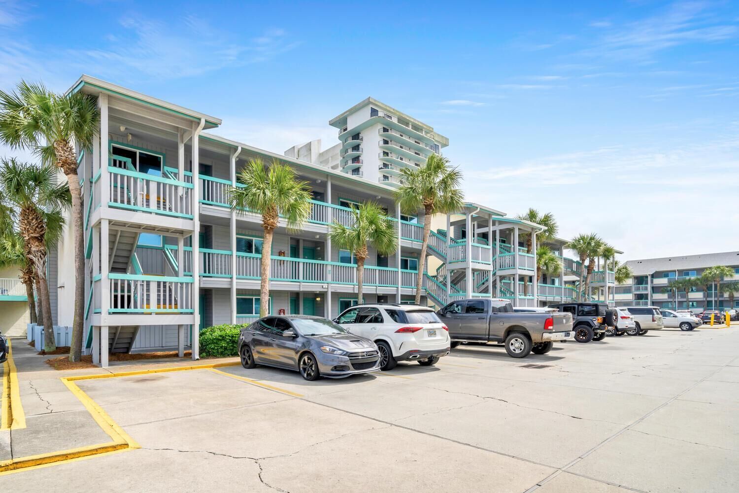 A multi-story hotel with balconies, parking spaces, and palm trees.