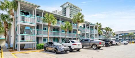 A multi-story hotel with balconies, parking spaces, and palm trees.