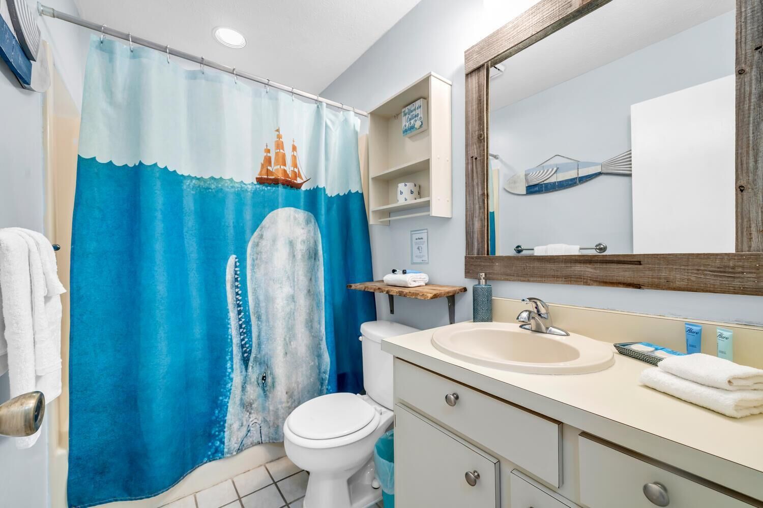 Un baño con un espejo grande, un lavamanos, un inodoro y una cortina de ducha con diseño de ballena.