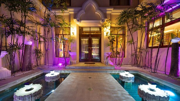 A pool area with a central pathway, surrounded by stone planters and tropical plants.