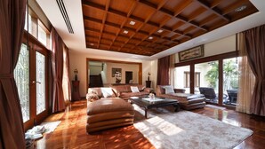 A spacious living room with a wooden ceiling, leather sofas, a coffee table, and large windows with curtains.