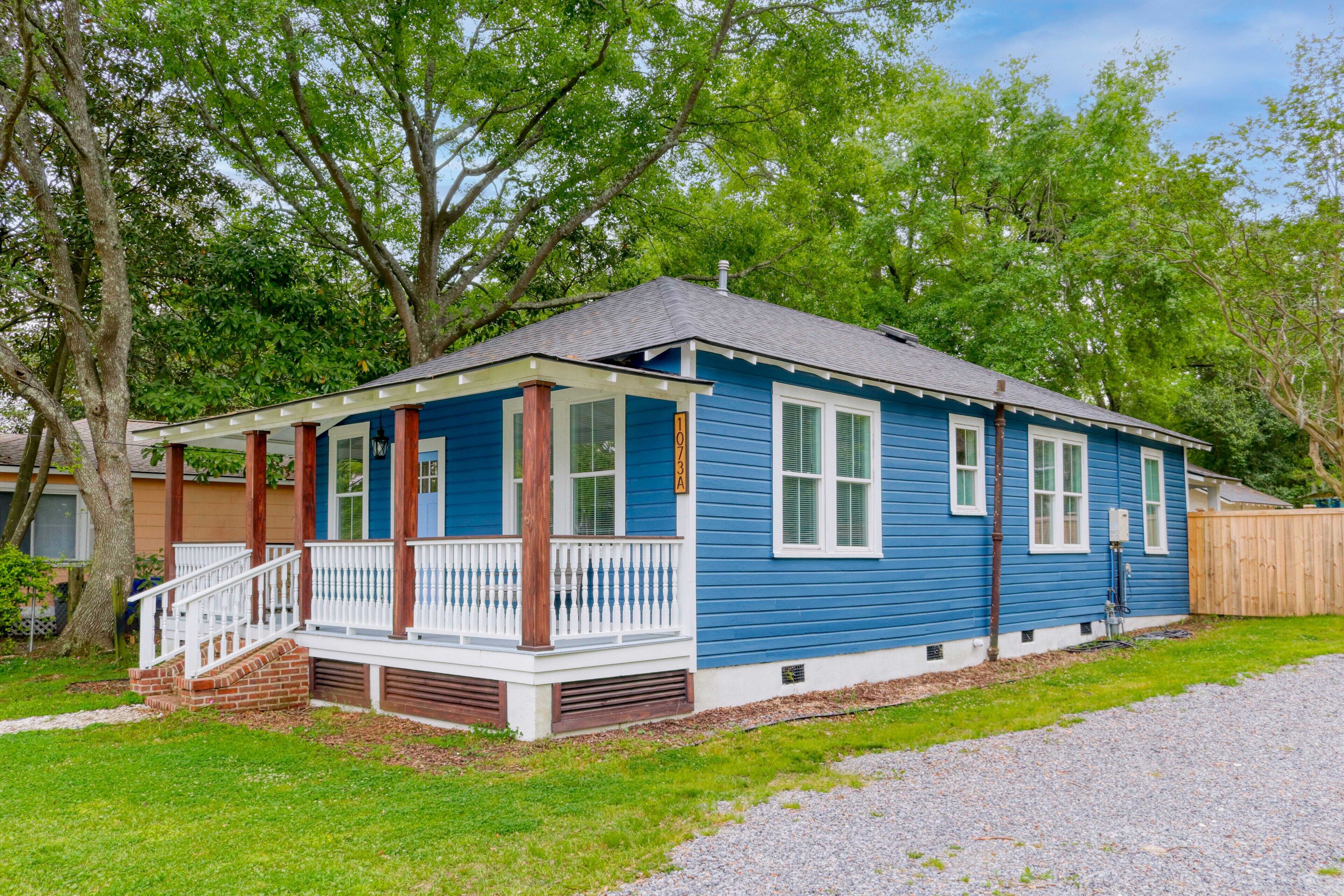 A single-story blue house with a front porch, white shutters, and a wooden fence.