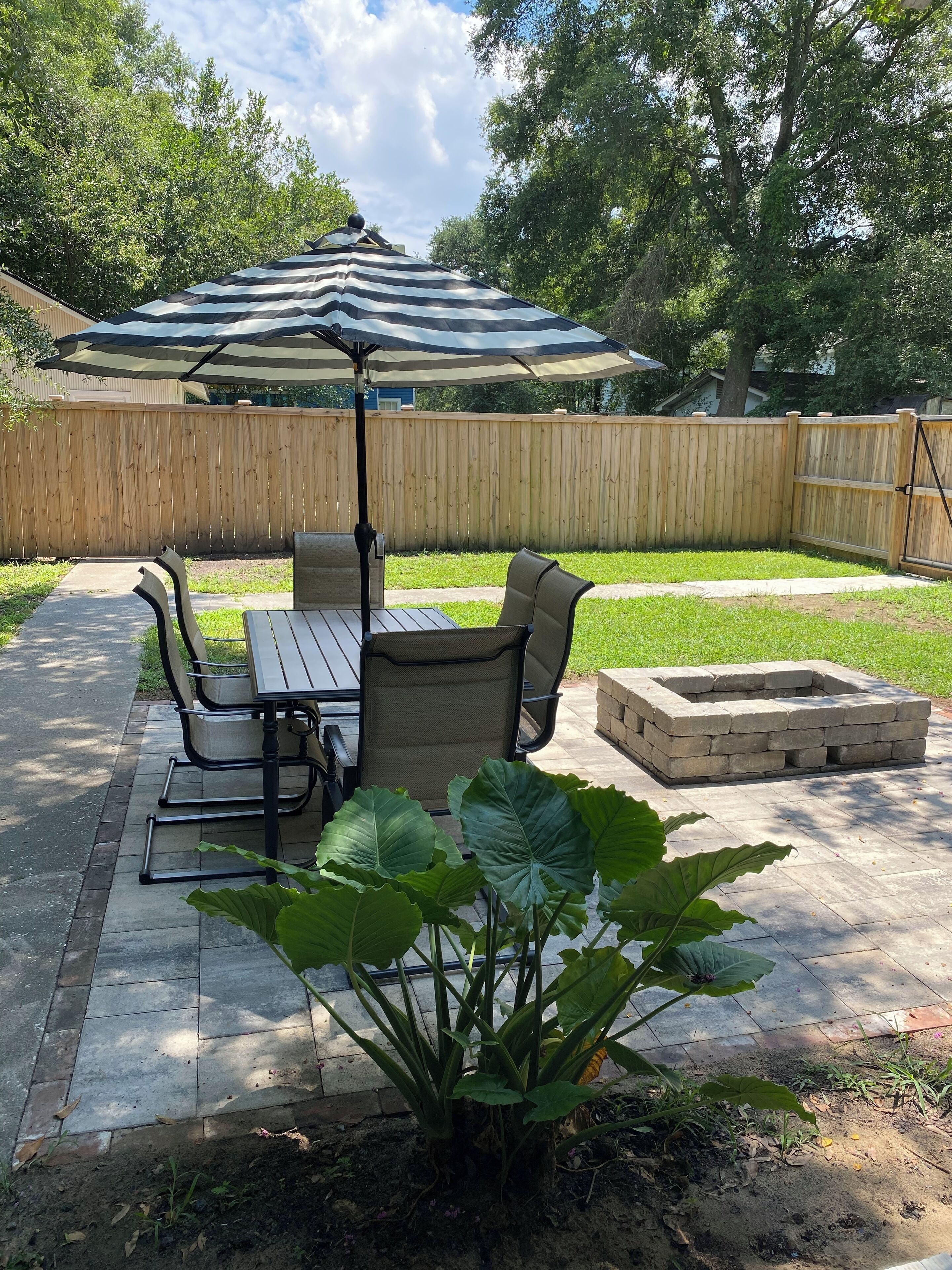 A patio area with a table and chairs, a large umbrella, and a fire pit.