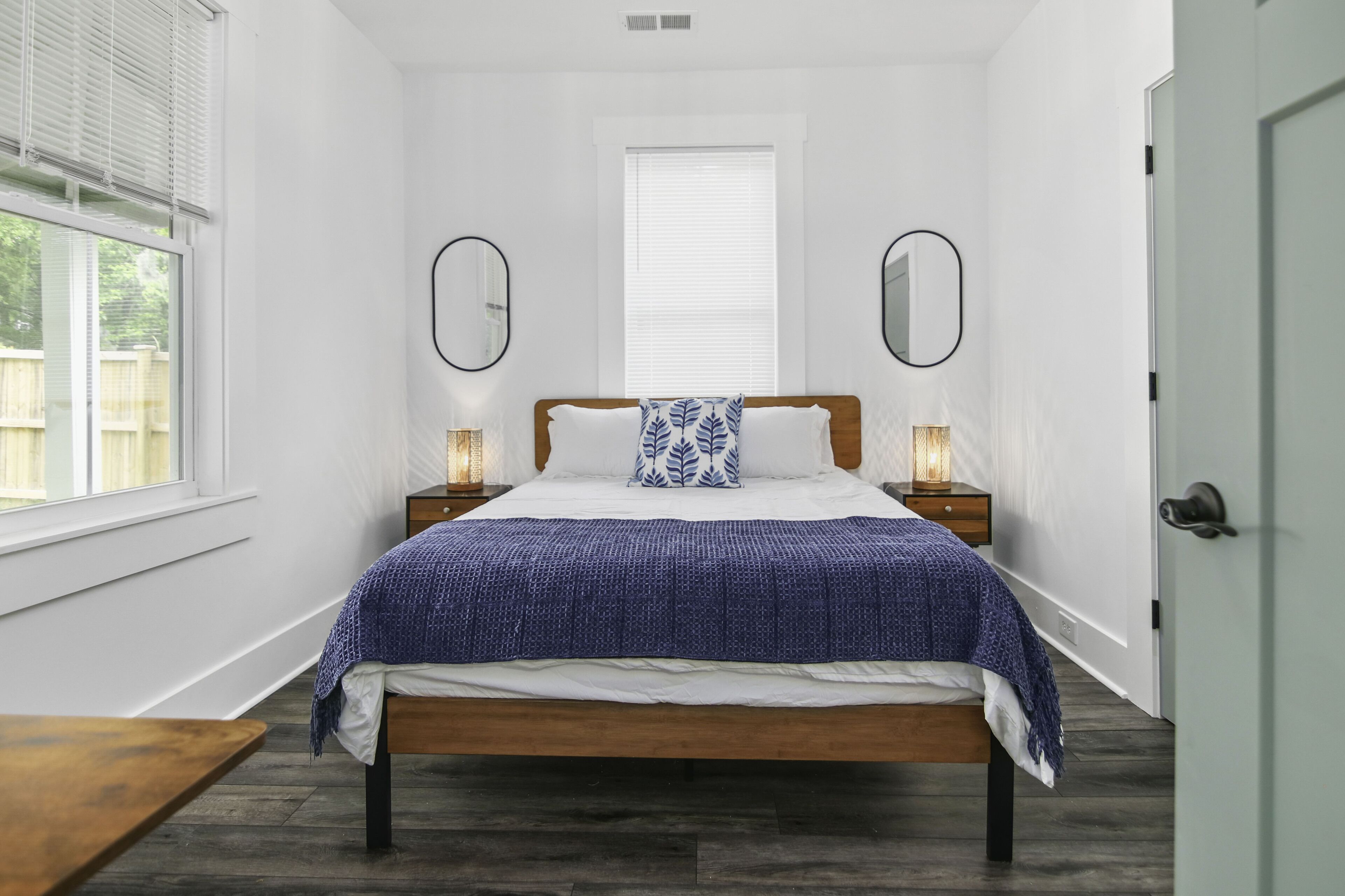 A bedroom with a wooden bed, white walls, a window, and two bedside lamps.