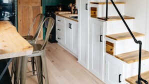 Een moderne keuken met houten kastjes, een eethoek met metalen stoelen en een trap met zwarte leuningen.