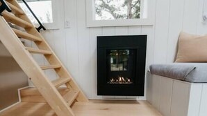 A room with a wooden staircase, a fireplace, and a sofa. - Tiny Home Near Wine Country with Stargazing Loft (Hastings County)