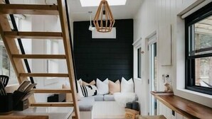 A modern interior with a wooden ladder, a black accent wall, and a cozy seating area with cushions. - Tiny Home Near Wine Country with Stargazing Loft (Hastings County)