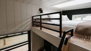 A bunk bed room with a wooden headboard, white walls, and a window providing natural light. - Tiny Home Near Wine Country with Stargazing Loft (Hastings County)