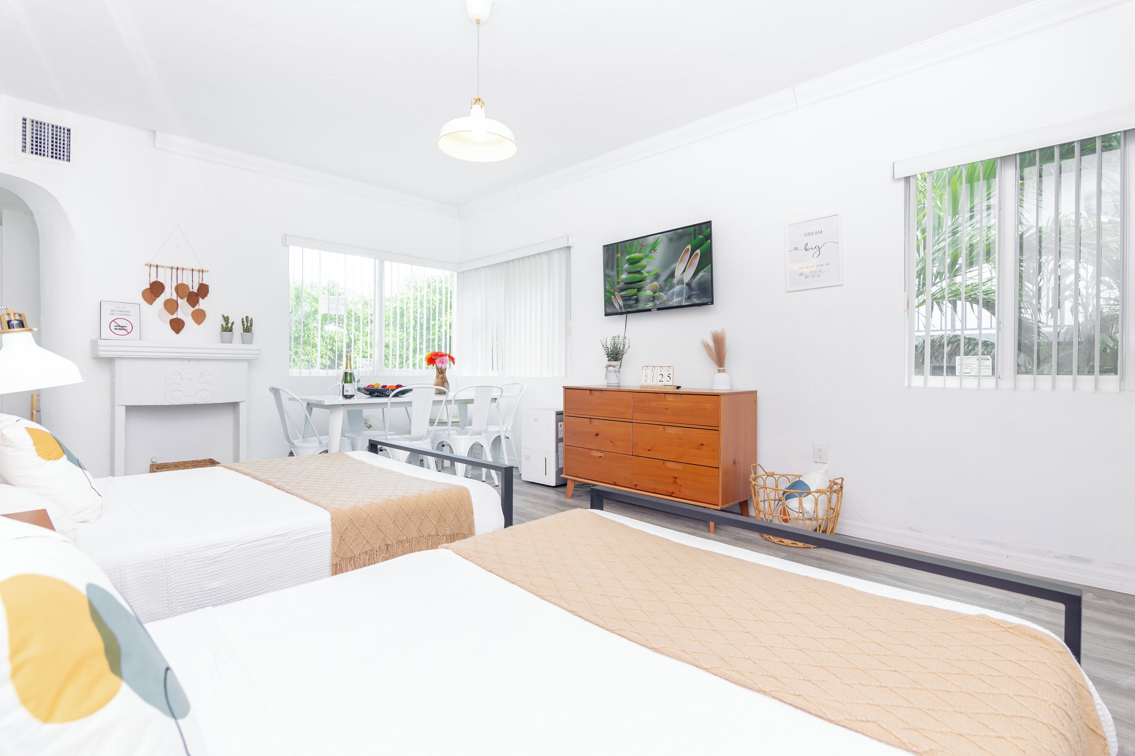 A modern hotel room with two beds, a desk, a dresser, and a TV.
