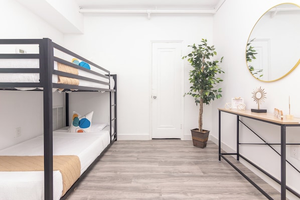 A bunk bed room with a wooden floor, a potted plant, a mirror, and a small table with decorative items. - West Deco Boutique Apartments (Miami Beach)