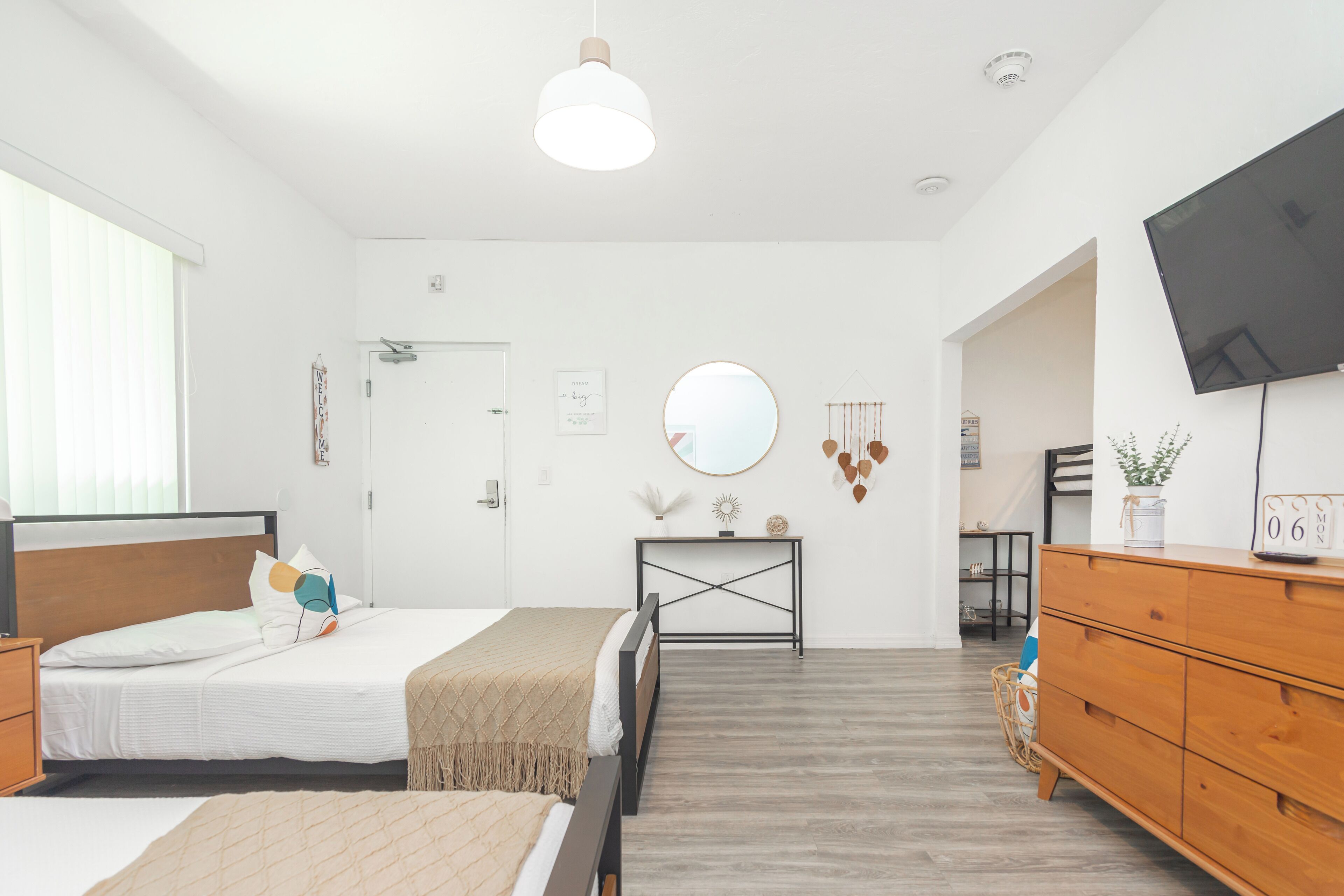 A modern bedroom with a bed, bedside tables, a dresser, a TV, and a mirror on the wall.