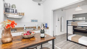 A modern kitchen with a wooden table, a vase of flowers, a bottle of champagne, and a fruit bowl. - West Deco Boutique Apartments (Miami Beach)