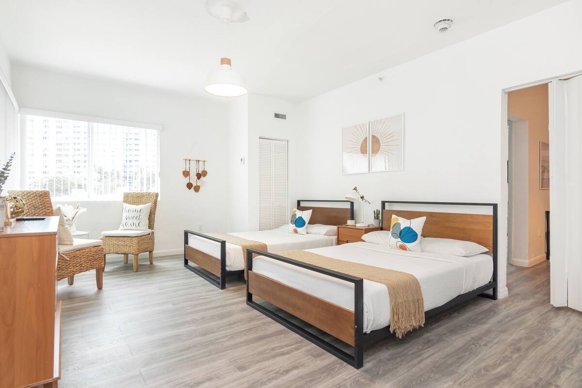 A modern hotel room with two beds, a desk, and a chair.