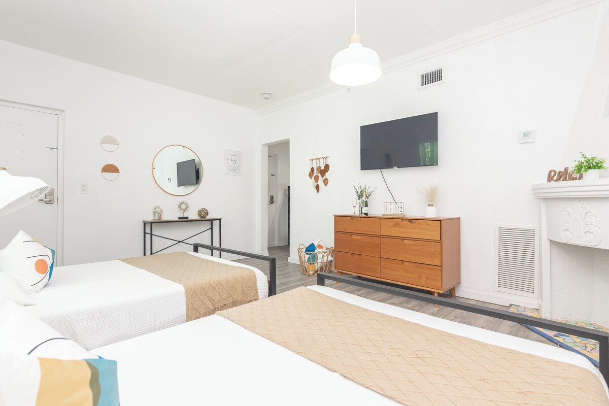 Een moderne hotelkamer met twee bedden, een houten dressoir, een televisie en een open haard.