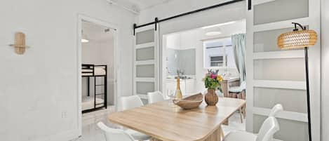 A modern dining area with a wooden table, white chairs, and a hanging light fixture.