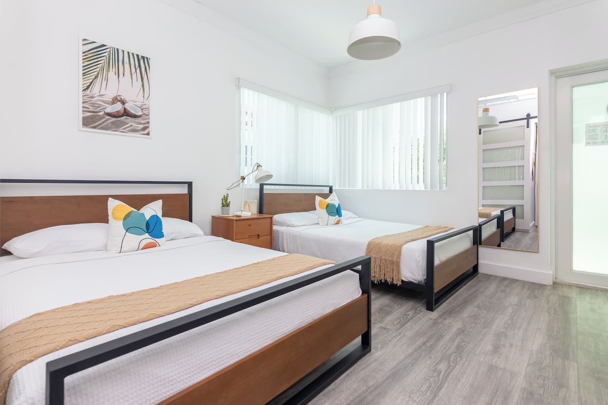 A modern hotel room with two beds, a large window, a bedside table, and a wall-mounted artwork.