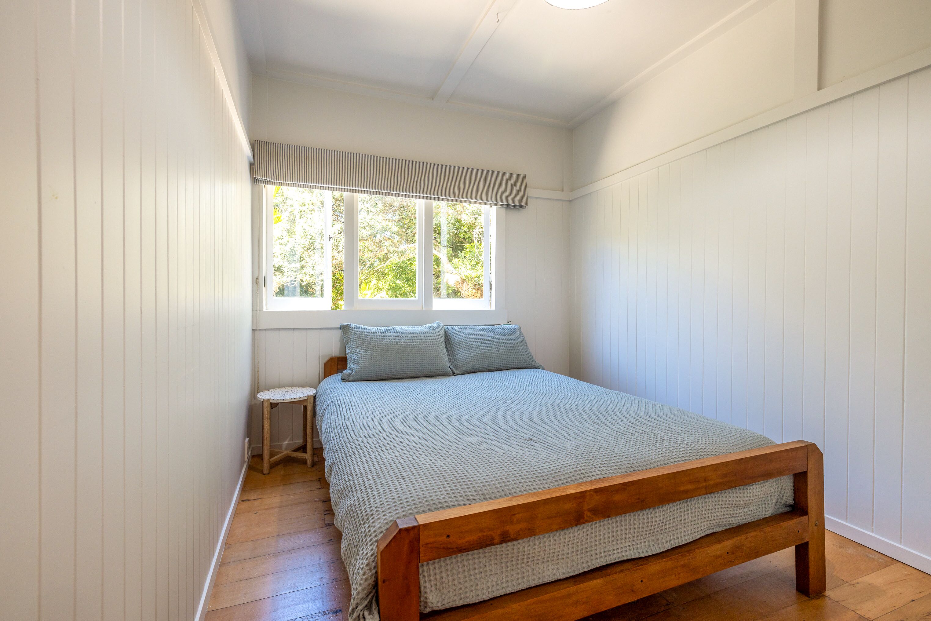 Une chambre avec un lit en bois, une petite table de chevet et une fenêtre donnant sur un paysage verdoyant.
