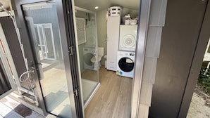 A compact, modern bathroom with a glass door, a washing machine, and a toilet.