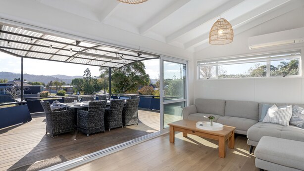A spacious living area with a large glass door leading to an outdoor deck, a grey sofa, and wicker furniture.