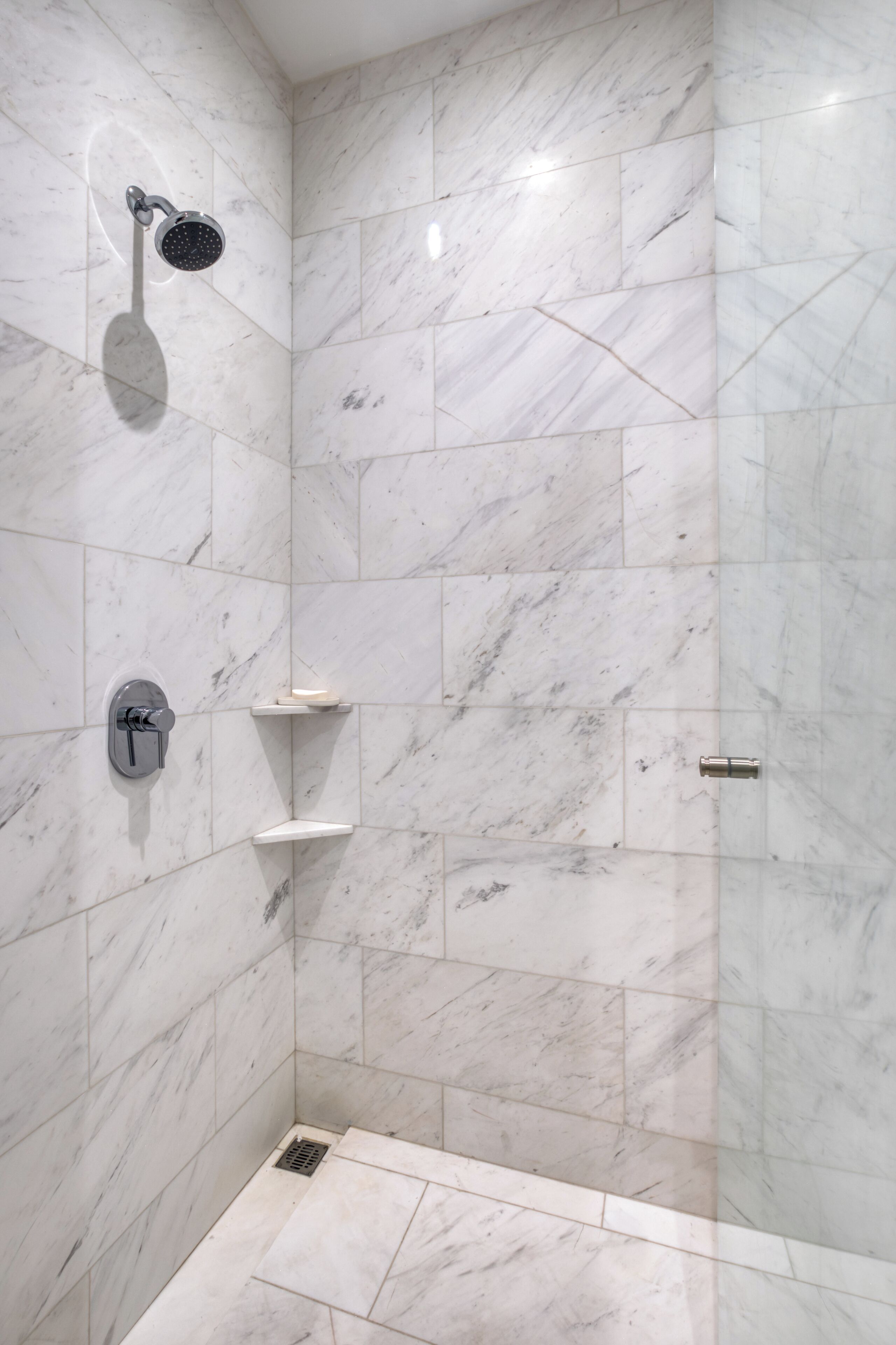 A modern shower with a handheld showerhead, a wall-mounted control, and a small shelf.