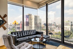 A modern living room with a black leather sofa, a round coffee table, and a view of the city through large windows.