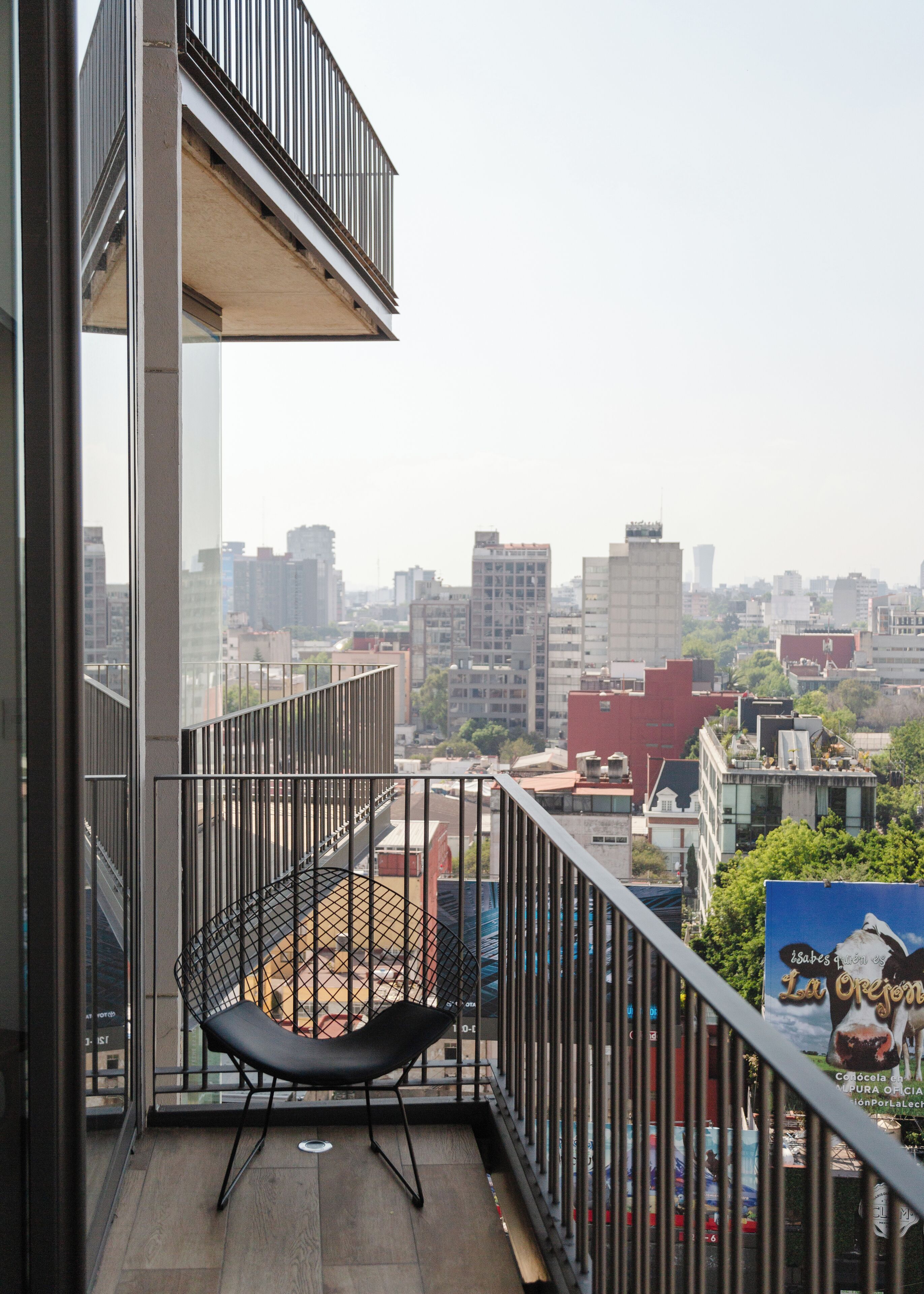 A balcony with a black chair, a view of a cityscape, and a poster on the railing.