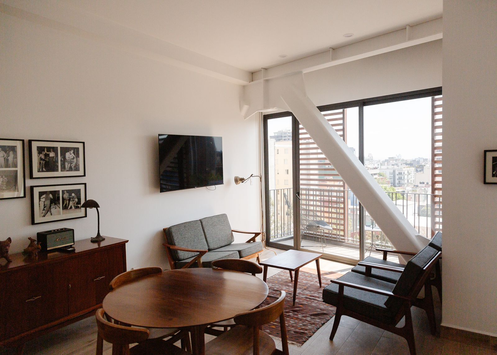 A spacious living room with a large TV, a dining table, and a balcony with a city view.