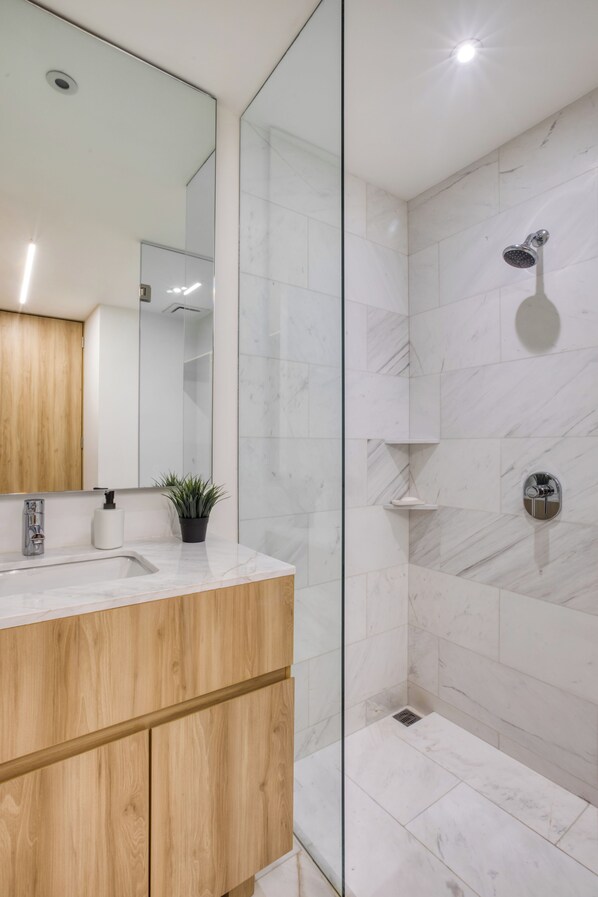 A modern bathroom with a wooden vanity, a glass shower enclosure, and marble tiles.