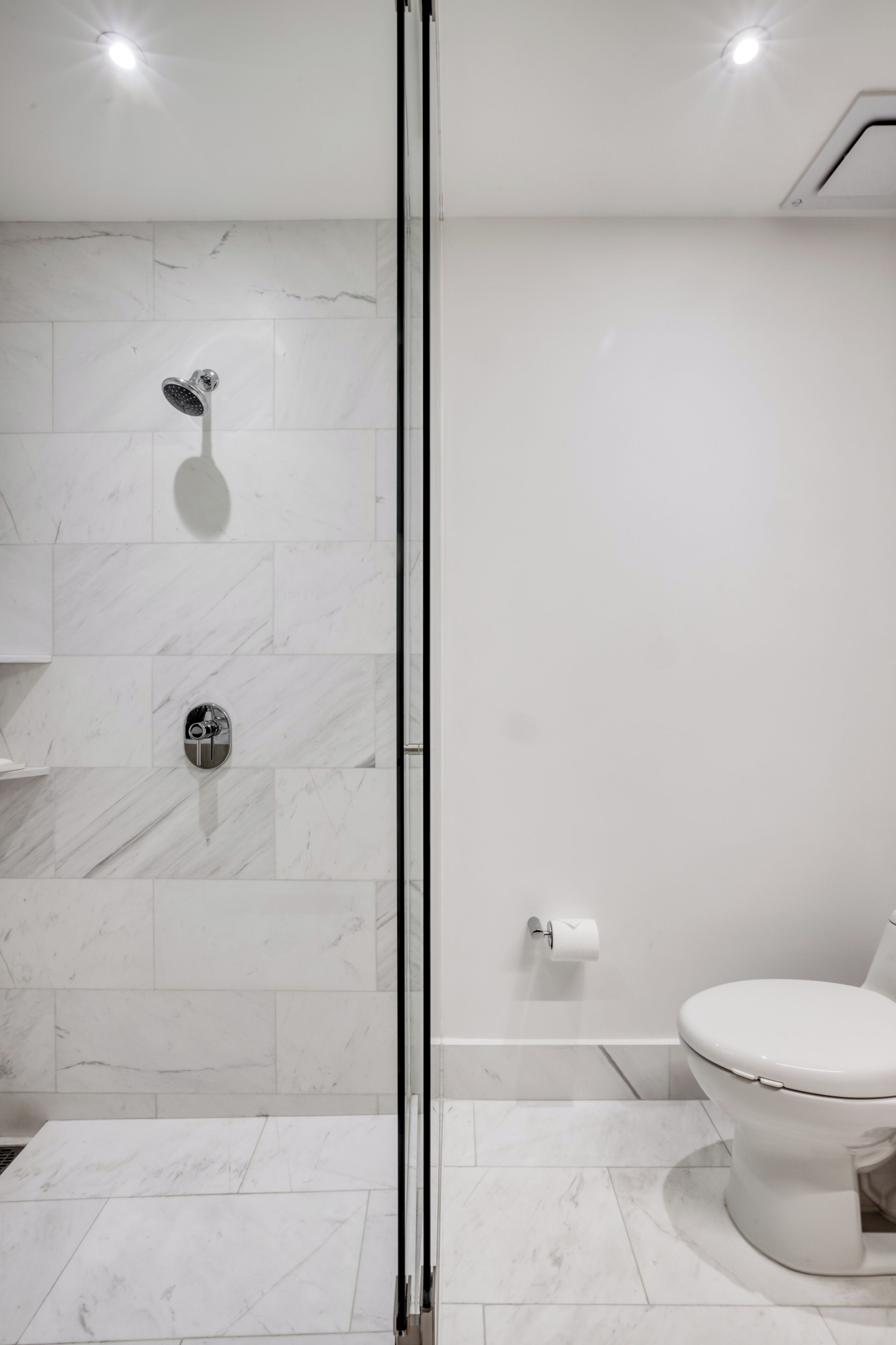Une salle de bain moderne dotée d’une douche à parois de verre, de toilettes et d’un sol carrelé en marbre.