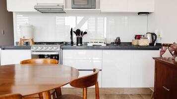 Una cocina moderna con armarios blancos, estufa a gas, microondas y comedor con mesa y sillas de madera.