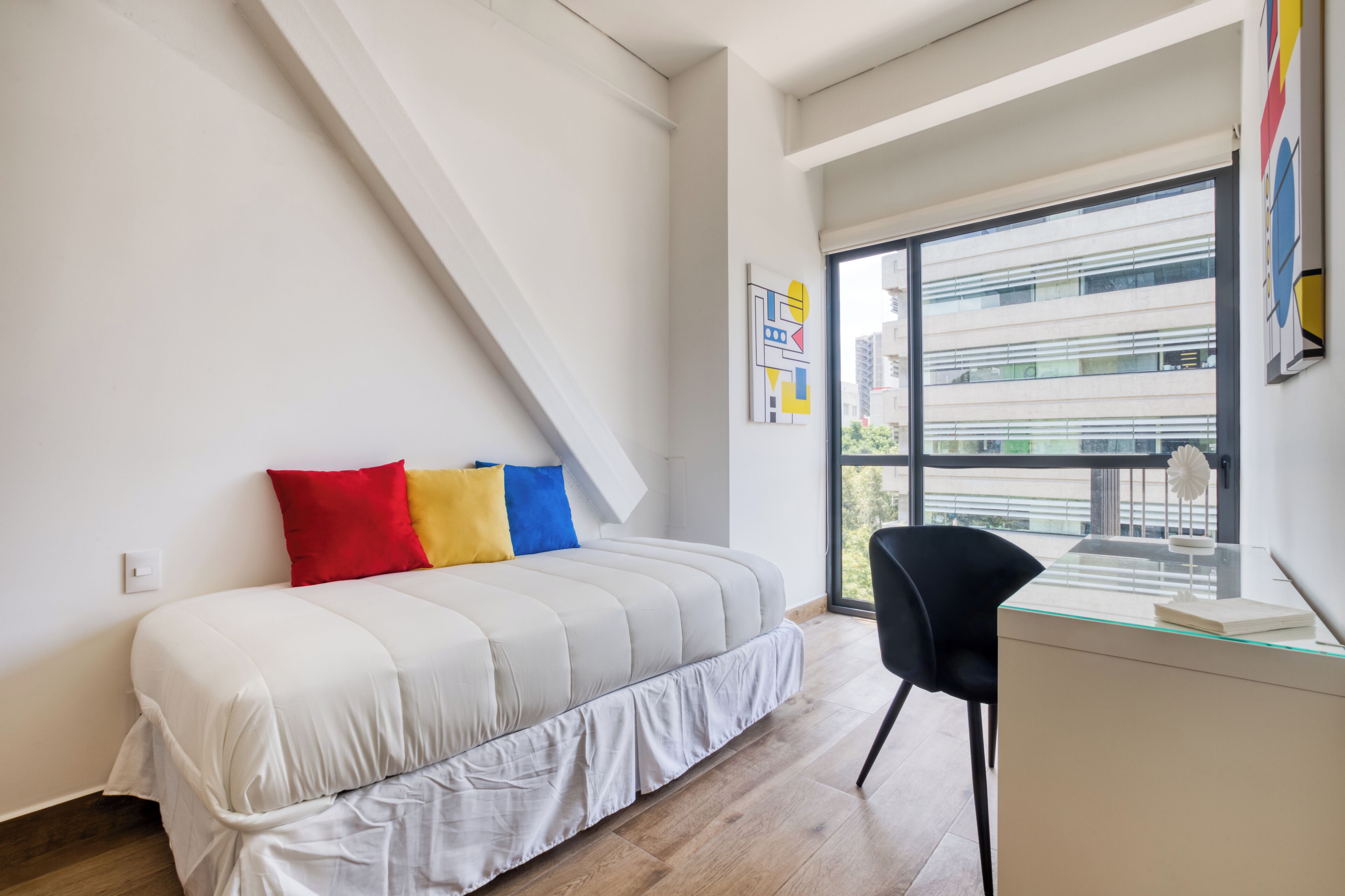 A modern bedroom with a bed, a desk, and a large window.