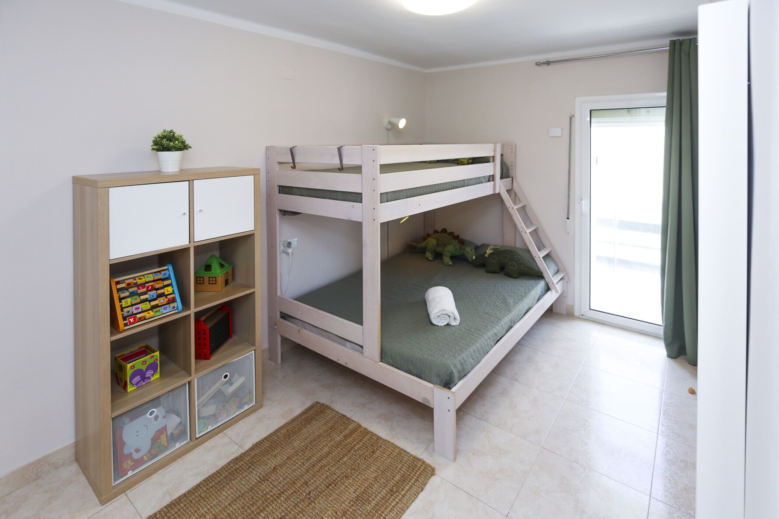 A bunk bed with a ladder, a wooden cabinet with storage drawers, and a small plant on top.