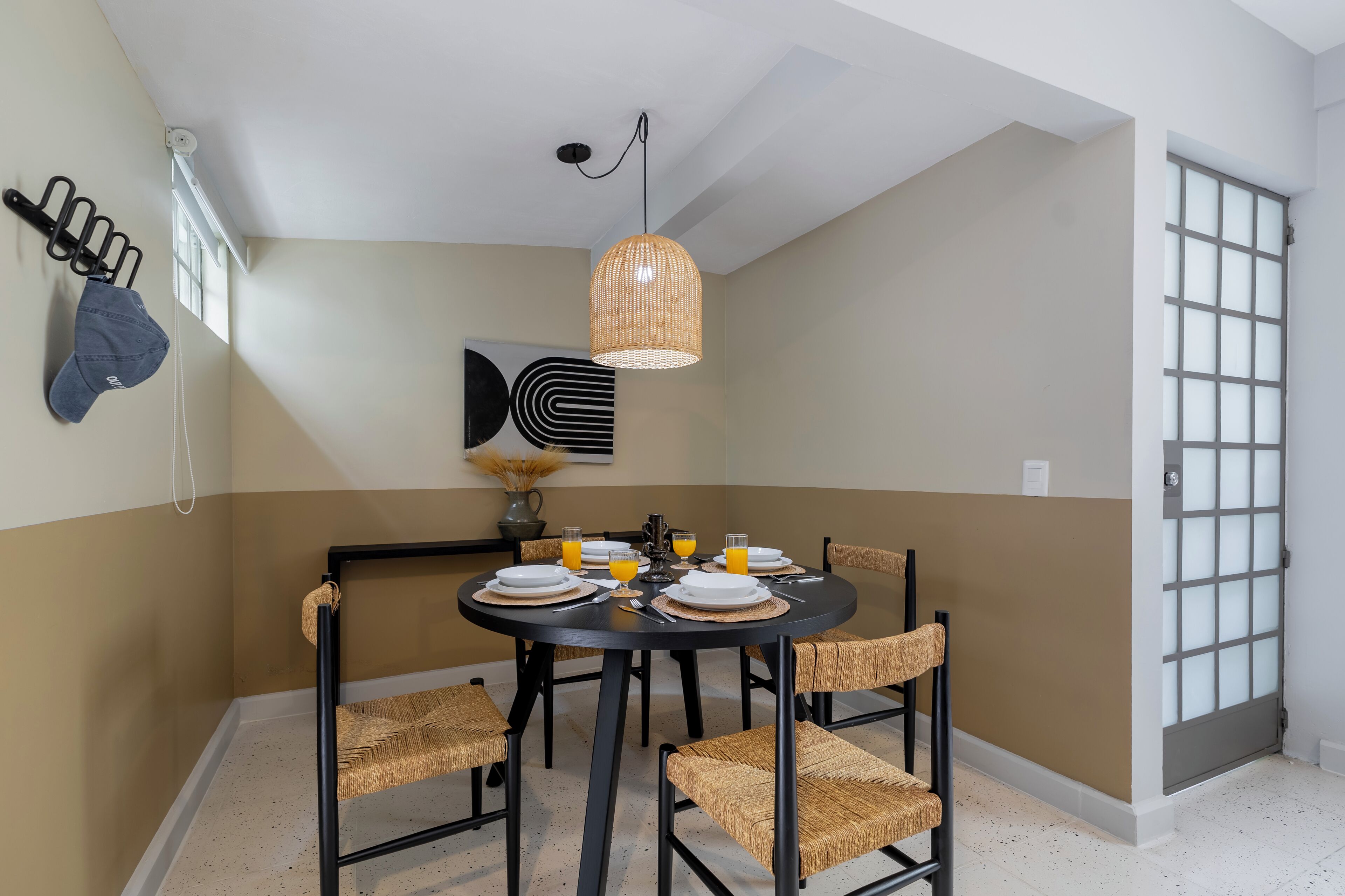 Un coin repas avec une table ronde dressée pour quatre personnes, entourée de chaises en osier.