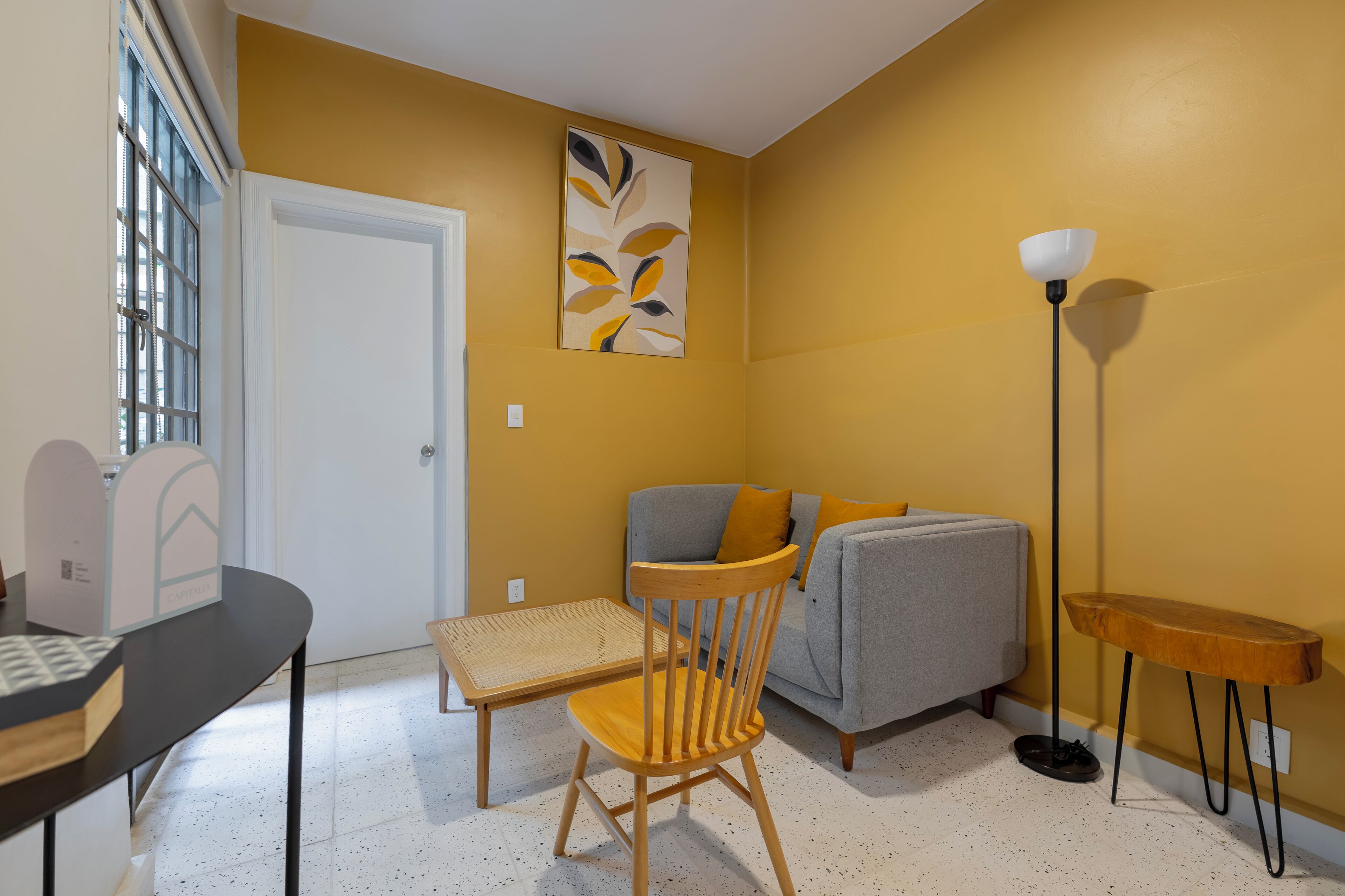 A room with a wooden chair, a grey sofa, a small table, and a floor lamp.