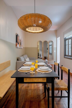 Un comedor con una mesa negra dispuesta para cuatro personas, rodeada de sillas con asientos de mimbre. Una lámpara colgante grande de mimbre cuelga sobre la mesa.