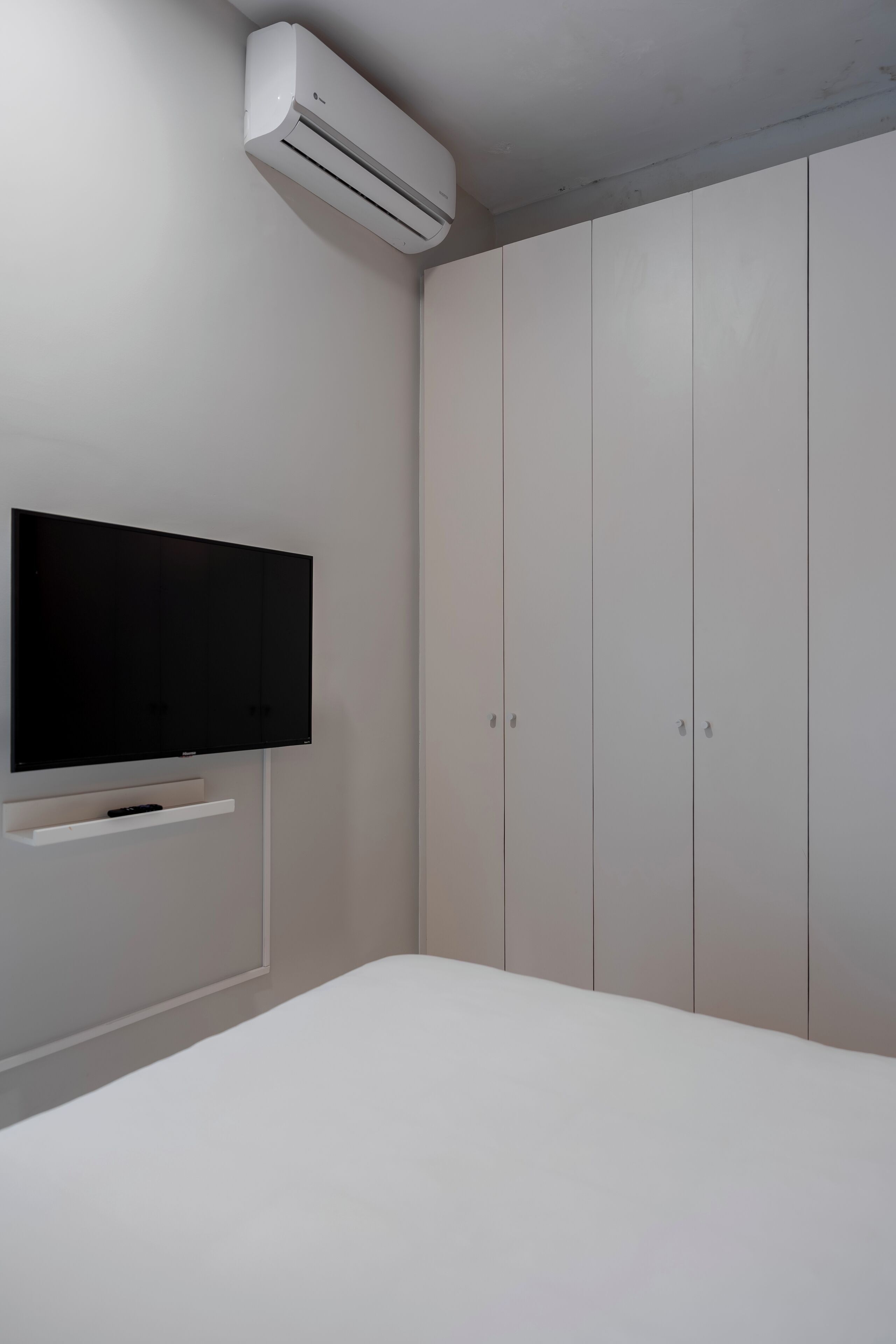 Ein Schlafzimmer mit einem Bett, einem an der Wand befestigten Fernseher und einem Kleiderschrank.