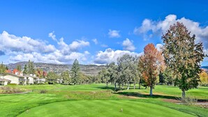 Um campo de golfe com grama bem cuidada, céu claro e montanhas ao fundo.