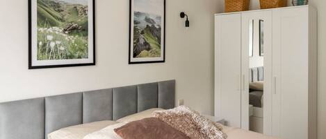 A bedroom with a bed, two framed pictures, a wardrobe, and a nightstand with a lamp.