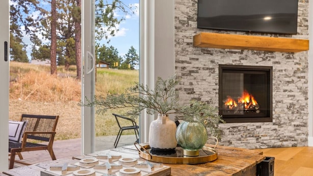 A modern living room with a fireplace, wooden furniture, and a view of a grassy field.