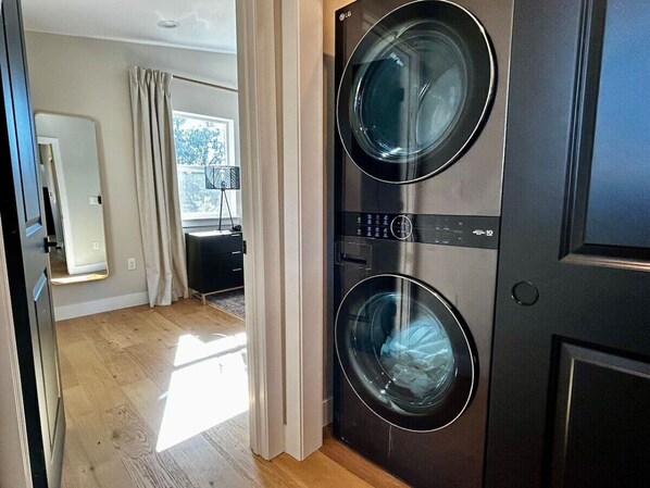 A laundry room with two front-loading washing machines, a mirror, and a window with curtains. - Serene Mountain Luxury-King beds & private Hot tub (Bailey)