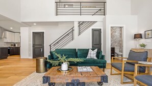 A spacious living area with a green sofa, a wooden coffee table, and a staircase leading to an upper level.