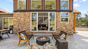 A modern two-story house with a stone exterior, large windows, and a fire pit in the patio area.