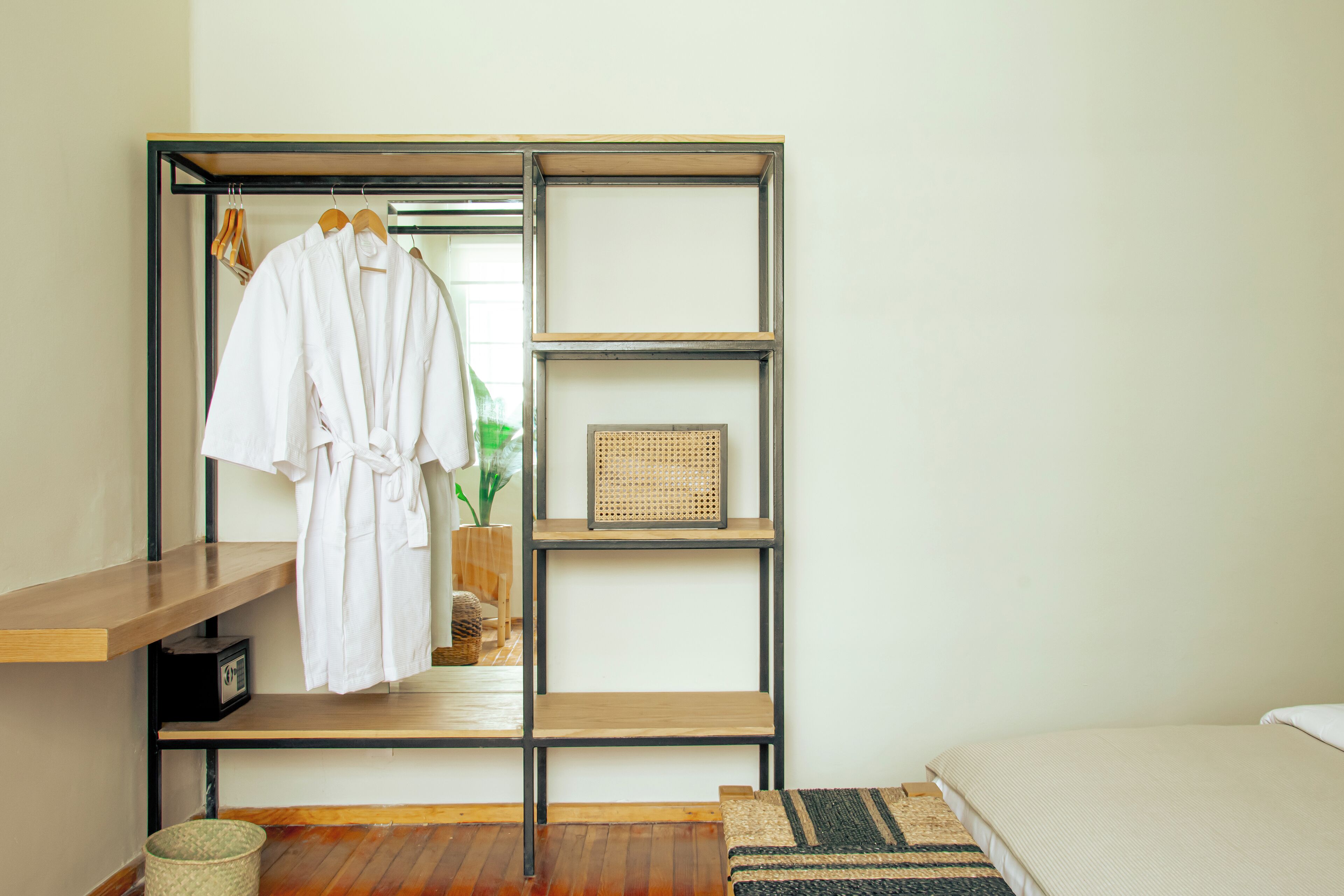 A bedroom with a wooden bed, a bedside table, a wardrobe with a mirror, and a hanging robe.