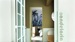 Un couloir avec un lit, une chaise en osier et un mur orné d’une enseigne indiquant « Candaria ».