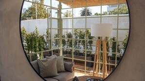 Une vue circulaire d’une pièce comprenant un canapé, une lampe et une table, donnant sur un jardin avec des plantes et un mur blanc.