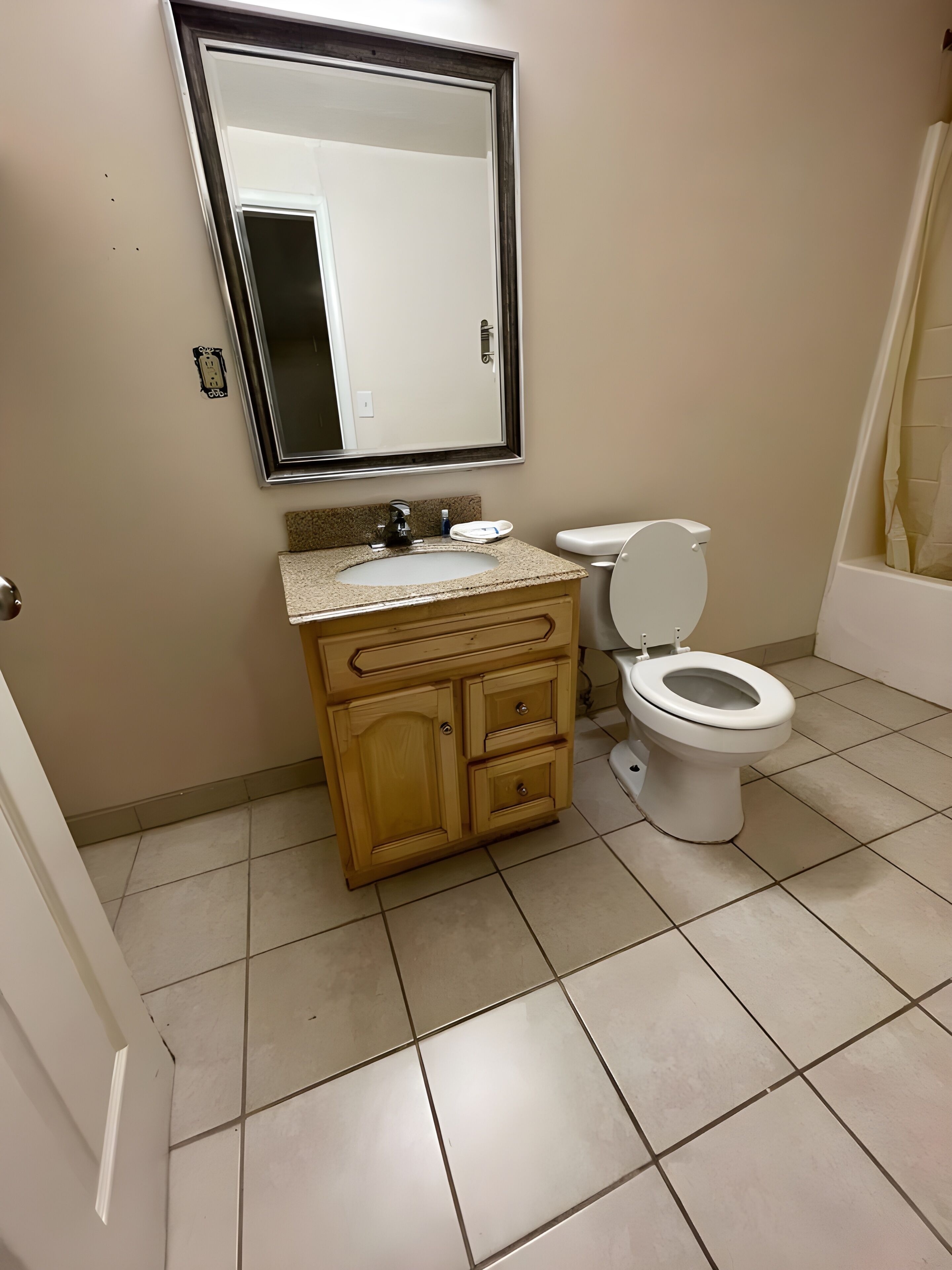 Un baño con inodoro, lavabo, espejo y suelo de baldosas.
