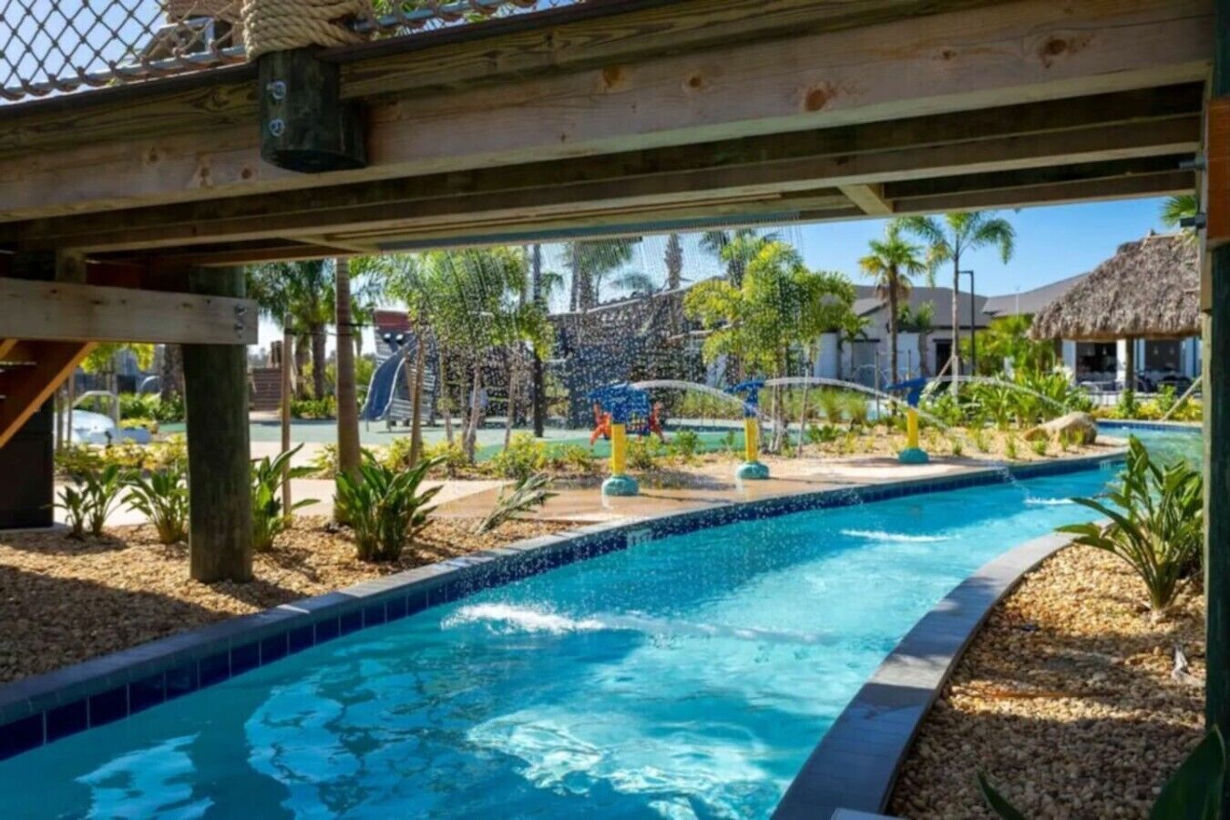A swimming pool with a water feature, surrounded by palm trees and a thatched-roof structure.