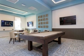 A room with a pool table, chairs, a TV, and artwork on the wall.