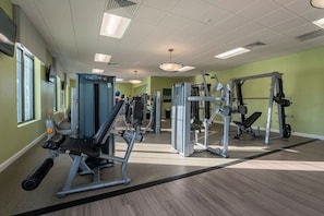 A gym with various exercise machines, a mirror, and a window on the left.